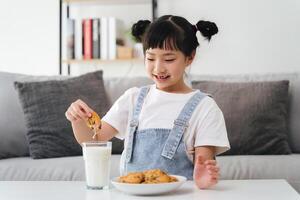 uma jovem menina é comendo biscoitos e bebendo leite foto