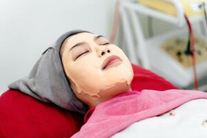 lindo jovem ásia mulher obtendo uma facial mascarar tratamento às a beleza salão. facial cuidados com a pele. foto