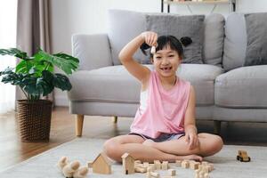 uma pequeno menina senta em a chão jogando com de madeira blocos foto