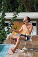 jovem homem desfrutando período de férias às a de praia e piscina foto