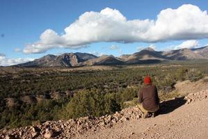 caminhante não identificado olhando para a montanha do alto deserto em uma estrada de terra foto