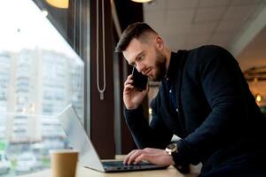 confiante homem de negocios discute problemas em a telefone e usa colo topo dentro uma cafeteria. ocupado homem trabalhando durante café pausa. fechar-se. foto