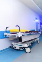 esvaziar médico carrinho em rodas em pé contra branco parede com azul listra dentro hospital câmara ou dentro corredor. fechar-se. foto
