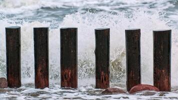 altos quebra-mares de madeira em ondas do mar espumantes foto