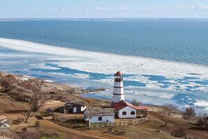 vista romântica atmosférica para o farol vermelho branco com casas de serviços agrícolas em merzhanovo foto