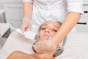 cosmetologista faz facial ultrassônico descamação para rejuvenescimento mulher face cuidados com a pele dentro beleza salão foto