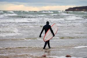 surfista masculino em traje de banho caminhando ao longo do mar com prancha de surf foto