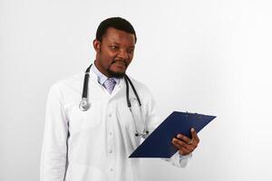 médico barbudo preto em manto branco com estetoscópio detém prontuário médico na área de transferência foto