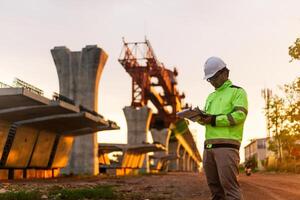 uma construção trabalhador é em pé em uma ponte, falando em dele célula telefone. a cena é conjunto dentro uma construção site, com uma ampla guindaste dentro a fundo. a trabalhador é vestindo uma amarelo Jaqueta foto