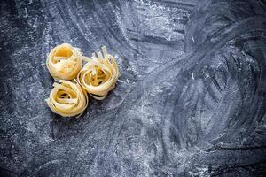 cru tagliatelle nido em a polvilhado com farinha Preto de madeira fundo foto