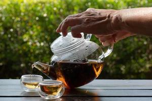 mulher servindo chá quente do bule na xícara de chá no jardim foto