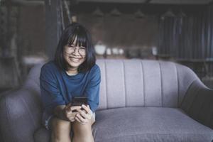 adolescente asiático com dentes sorrindo e segurando o smartphone na mão