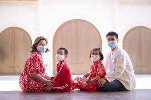Família asiática vestindo terno chinês vermelho e máscara de proteção sentada ao ar livre foto