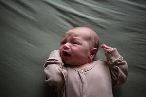 misturado raça recém-nascido bebê deitado com boca Largo aberto em verde algodão fralda vestido dentro bege maiô foto