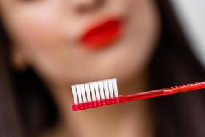 cortada retrato do lindo jovem mulher com escova de dente dentro mãos. saudável branco dentes e dental conceito. irreconhecível mulher às a borrado fundo foto