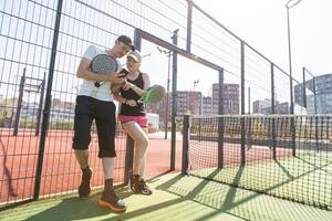 alegre Atlético casal rindo durante padel tênis Combine em ao ar livre tribunal. foto