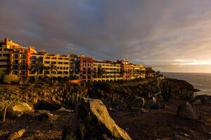 panorâmico Visão do a iluminado las Américas às noite contra a colorida pôr do sol céu com luzes em a horizonte em tenerife ilha, Espanha foto