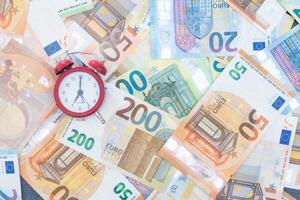 vermelho alarme relógio e euro notas do vários denominações em uma branco fundo. foto
