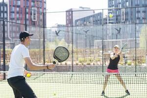jovem mulher jogando padel tênis com parceiro dentro a aberto ar tênis quadra foto