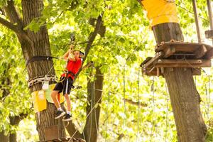 menina adorável aproveitando seu tempo no parque de aventura de escalada em um dia quente e ensolarado de verão foto