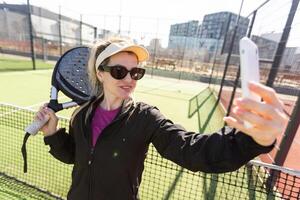 jovem fêmea sorridente e olhando às Câmera enquanto jogando padel contra verde fundo foto