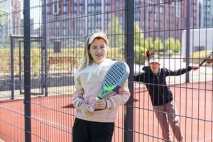 positivo mãe e filha em pé em quadra com padel raquetes foto