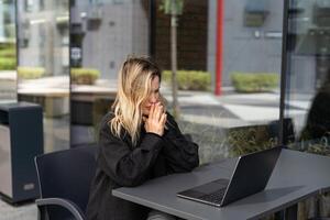 cansado jovem o negócio mulher dentro Preto terno com fones de ouvido é sentado com olhos fechadas dentro frente do computador portátil foto