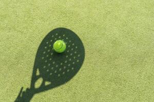 sombra do uma padel raquete com uma amarelo bola em a verde grama. foto