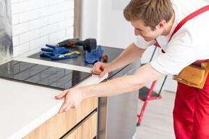 jovem reparador instalando indução fogão dentro cozinha. foto