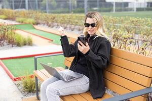 mulher em golfe curso com Smartphone com Esportes apostando aplicativo foto