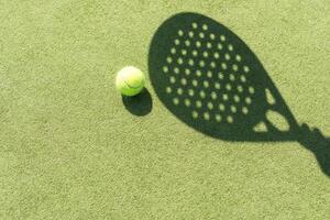 sombra do uma padel raquete com uma amarelo bola em a verde grama. foto