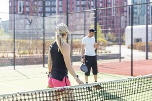 esportivo fino mulher com raquete jogando padel dentro tribunal. Visão a partir de a costas foto