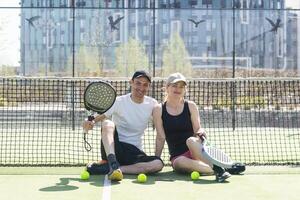 Esportes casal com padel raquetes posando em tênis quadra foto