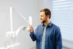 bonito masculino paciente olhando às dele lindo sorrir em pé às a dental escritório foto