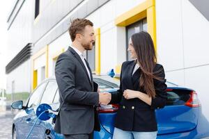 sorridente mulher em pé às a carro e apontando às carro vendedor tábua. ela é escolhido certo carro para dela ela Serra on-line. uma mulher conclui a acordo para Comprar uma carro e shakes a do gerente mão foto