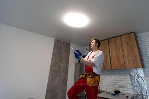 jovem homem instalando teto luminária em escada dentro cozinha foto
