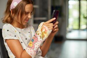 adolescente menina com uma quebrado braço ortopédico fundida usar Smartphone foto