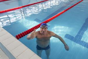uma feliz idosos homem carrinhos dentro uma piscina do limpar \ limpo água dentro a fresco ar em período de férias. foto