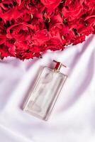 uma transparente chique perfume garrafa com uma delicado fragrância mentiras em uma branco cetim fundo. vermelho rosas ramalhete. topo visualizar. apresentação . em branco deitar. foto