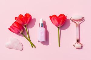 Cosmético conjunto para casa massagem e pele Cuidado do a face e pescoço. quartzo massageador, gua sha, natural óleo em uma Rosa fundo com flores plano deitar foto