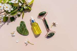 massageador, gua sha raspador , Cosmético massagem óleo dentro uma garrafa para casa massagem e facial pele Cuidado às lar. topo visualizar. uma ramo do uma floração árvore. foto