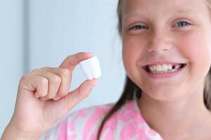 a criança detém uma plástico leite dente dentro dele mãos. a conceito do saudável dentes. foto