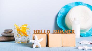 conceito Olá verão texto em cubos em coquetel fundo, protetor solar e chapéu em mesa foto
