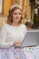 caucasiano mulher trabalhador autonomo senta em cidade rua usando computador portátil trabalhando conectados distante trabalho durante pausa foto