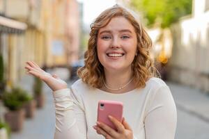 feliz ruiva menina usar Smartphone a comemorar ganhar Boa mensagem notícia loteria jackpot vitória ao ar livre foto