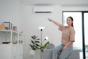 jovem mulher controlando ar condicionador às casa foto