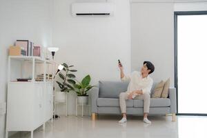 jovem homem desfrutando conforto usando controlo remoto ao controle para ar condicionamento às casa foto