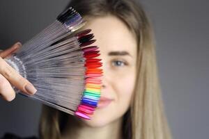 uma Loiras menina detém dentro dela mão uma paleta com amostras do unha esmaltes. ampla seleção do gel polonês cores. cor exibição em a anel. fechar-se foto