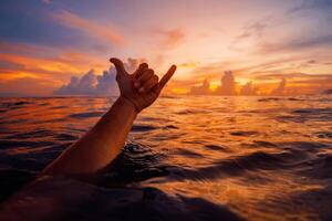 mão com shaka símbolo com brilhante pôr do sol dentro oceano. estilo de vida surfar conceito foto