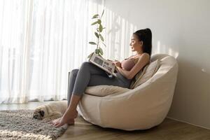 jovem ásia mulher lendo livro com pug cachorro dentro vivo quarto às casa foto